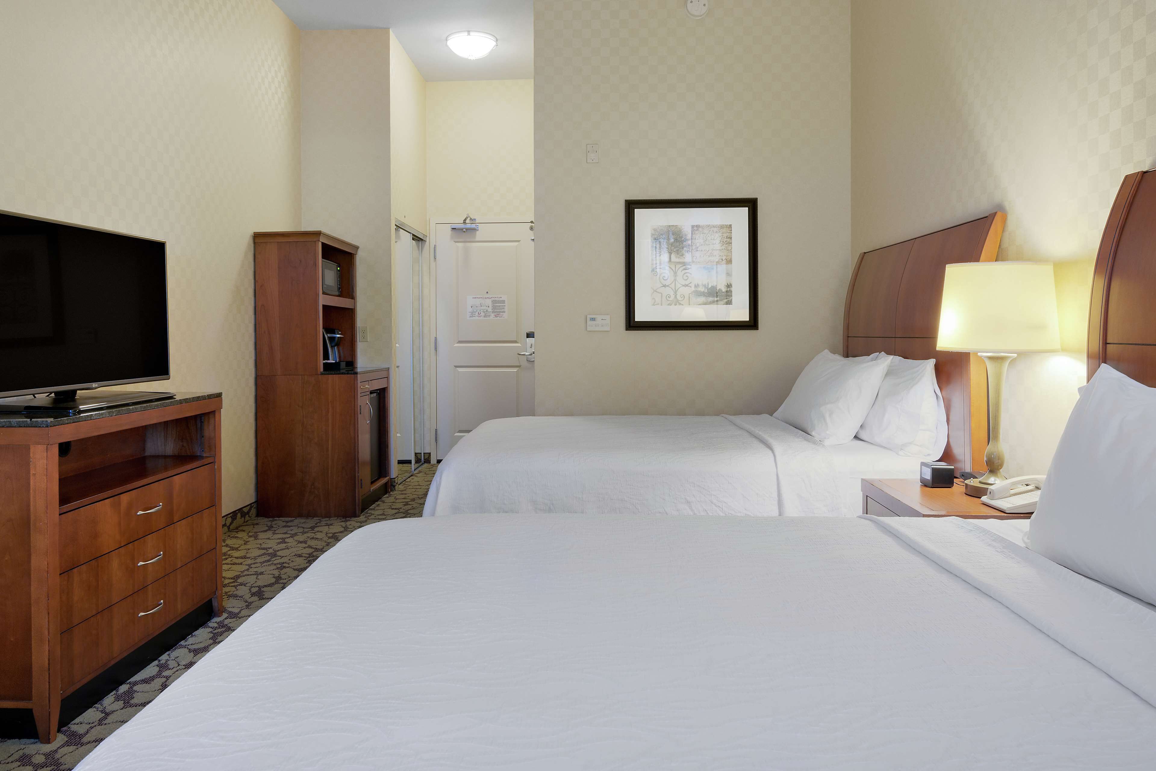 A hotel room with two beds, a TV, a wooden cabinet, and a framed picture on the wall.