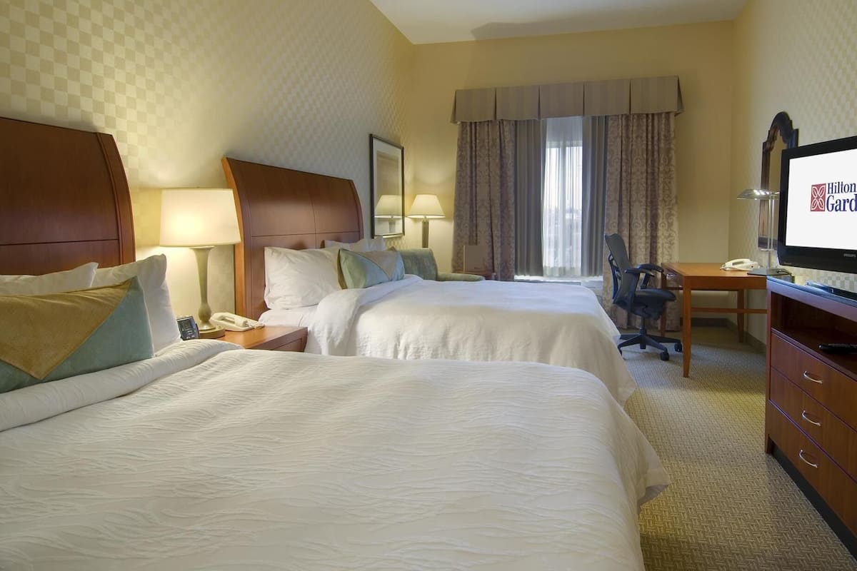 A hotel room with two beds, a desk, a chair, a television, and a window with curtains.