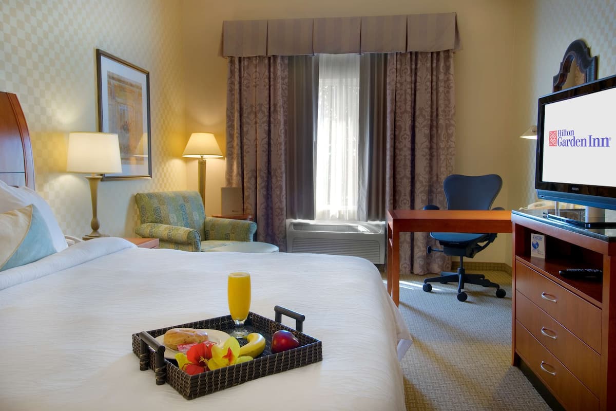 A hotel room with a bed, a desk, a chair, a television, and a tray with fruits and juice.