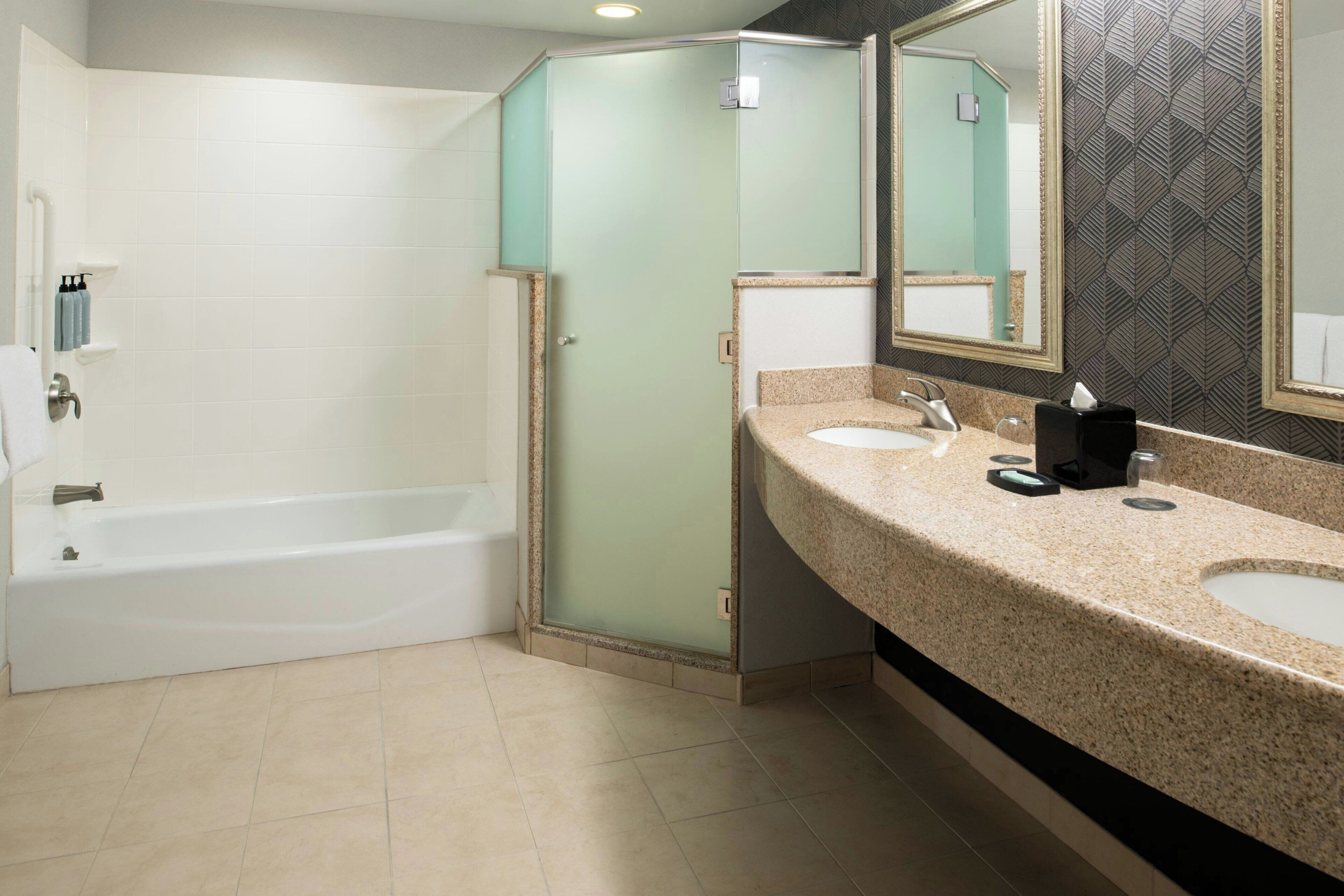 A bathroom with a bathtub, a glass shower enclosure, and a vanity with two sinks and a mirror.