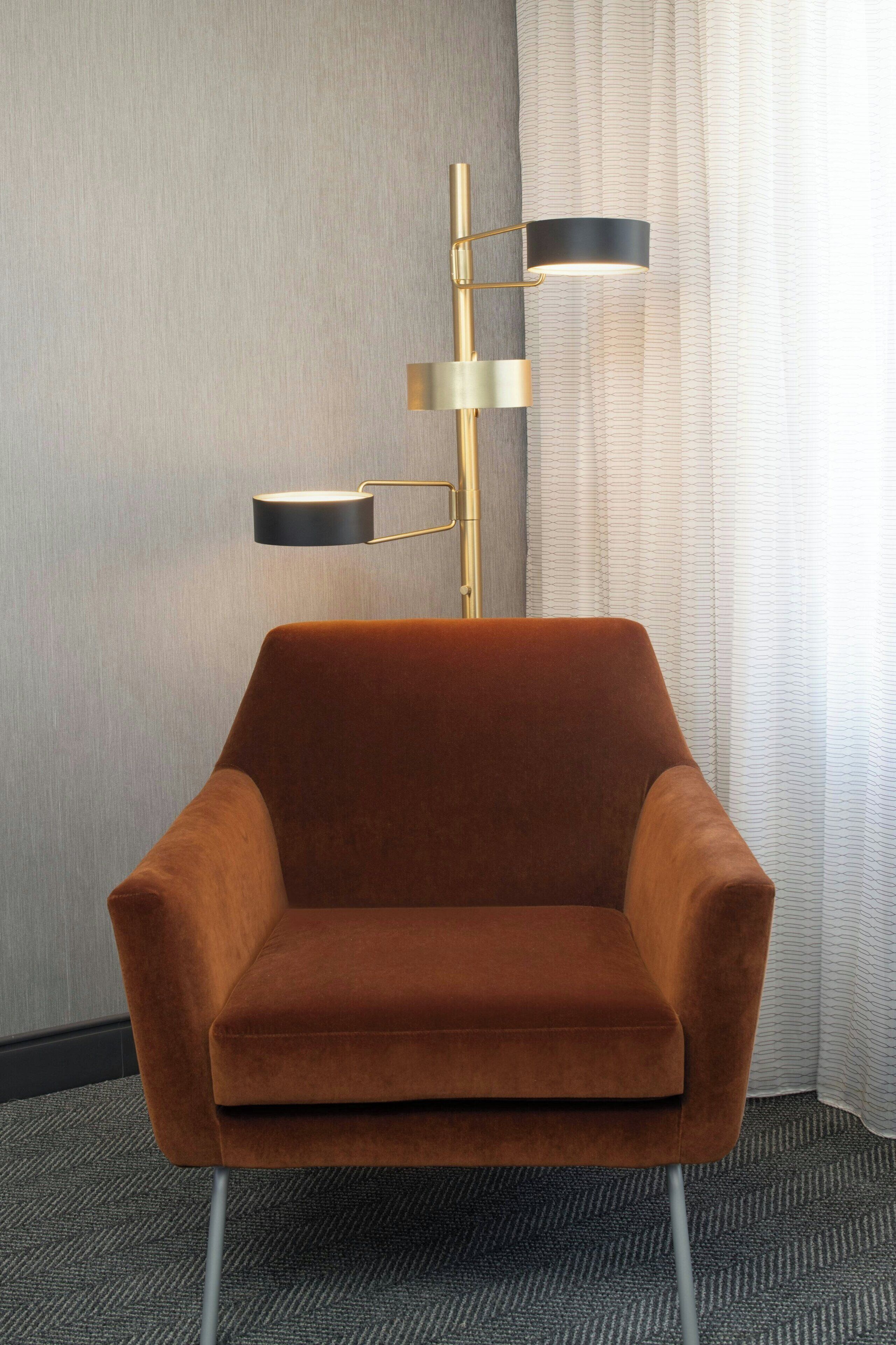 A modern room with a brown velvet armchair, a gold floor lamp, and a patterned curtain.