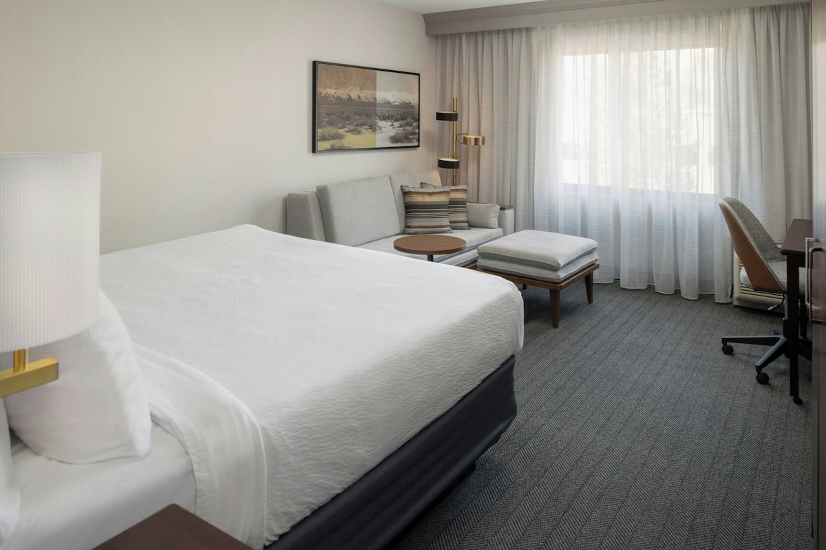 A hotel room with a large bed, a sofa, a desk, and a chair.