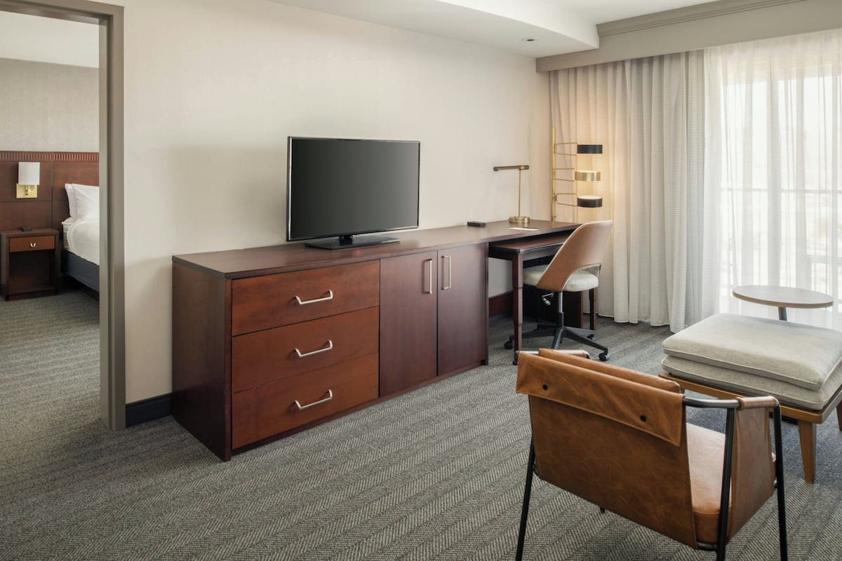 A hotel room with a wooden desk, a television, a chair, a small round table, and a sofa.