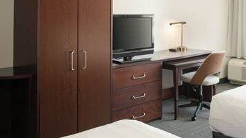 A hotel room with a wooden wardrobe, a desk with a television, a chair, and a bed.