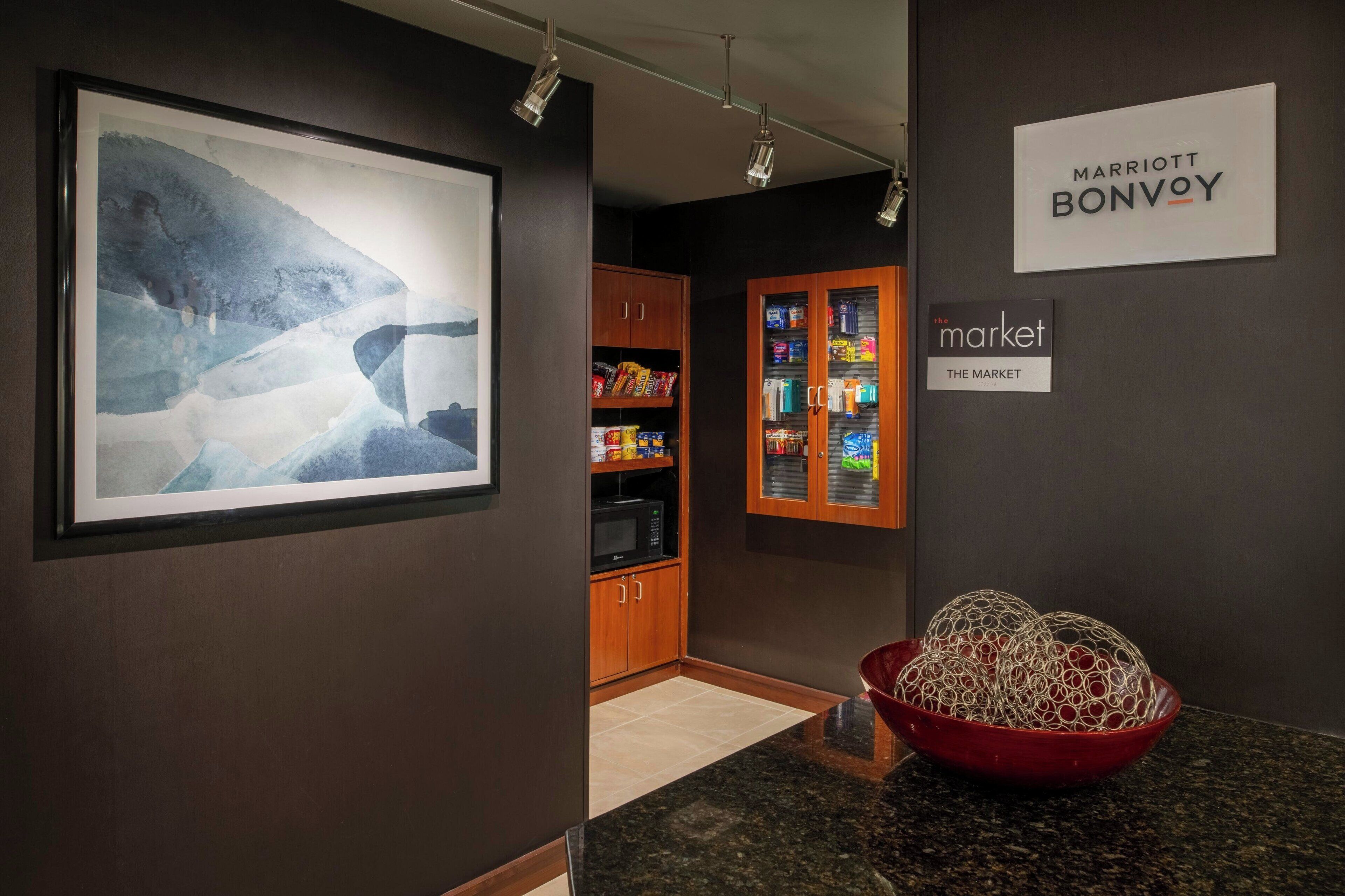 A hotel lobby with a framed abstract painting, a red decorative bowl, a kitchenette area, and signs for 'Marriott Bonvoy' and 'The Market'.