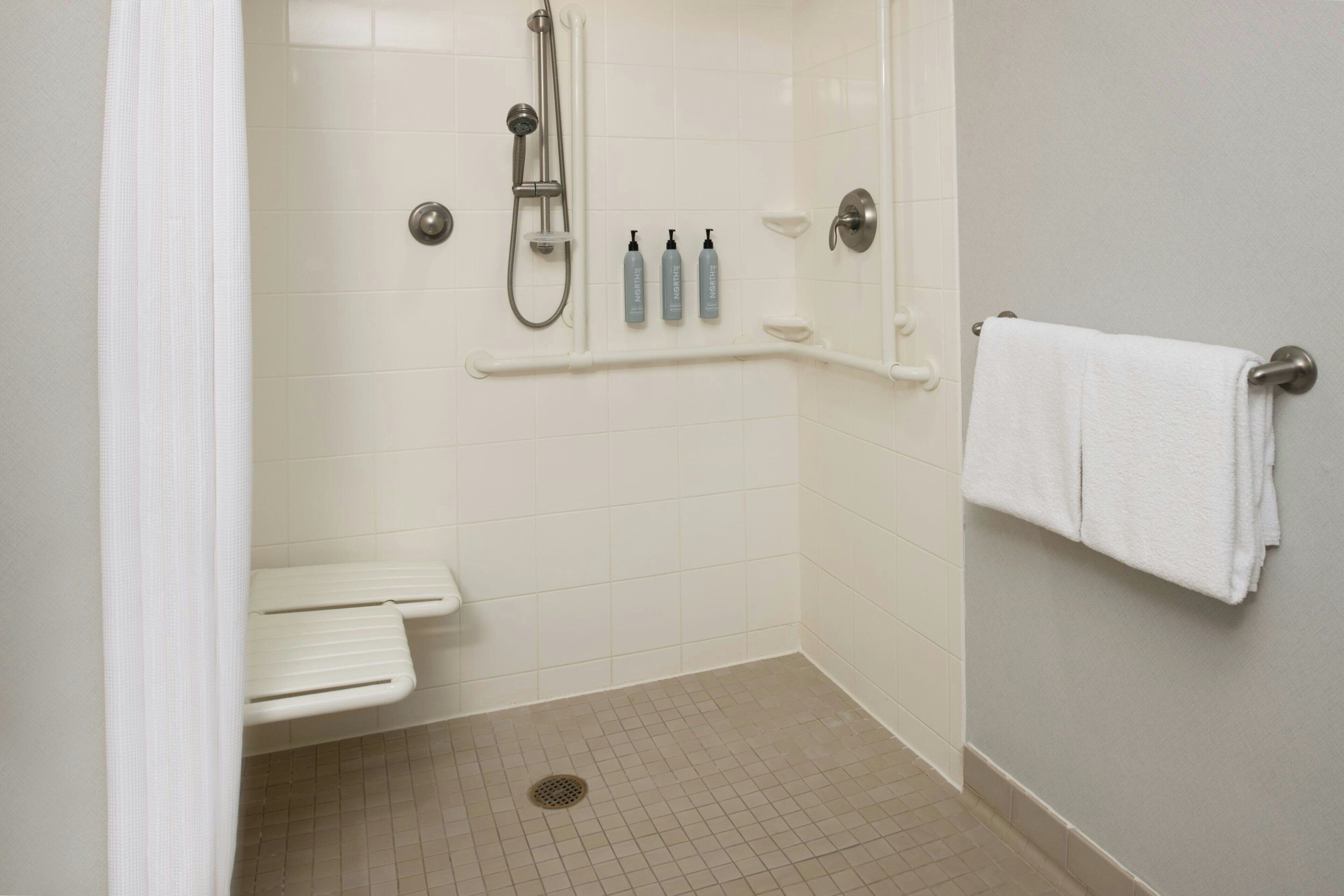 A small, clean shower area with a handheld showerhead, a shelf with toiletries, and a towel rack.