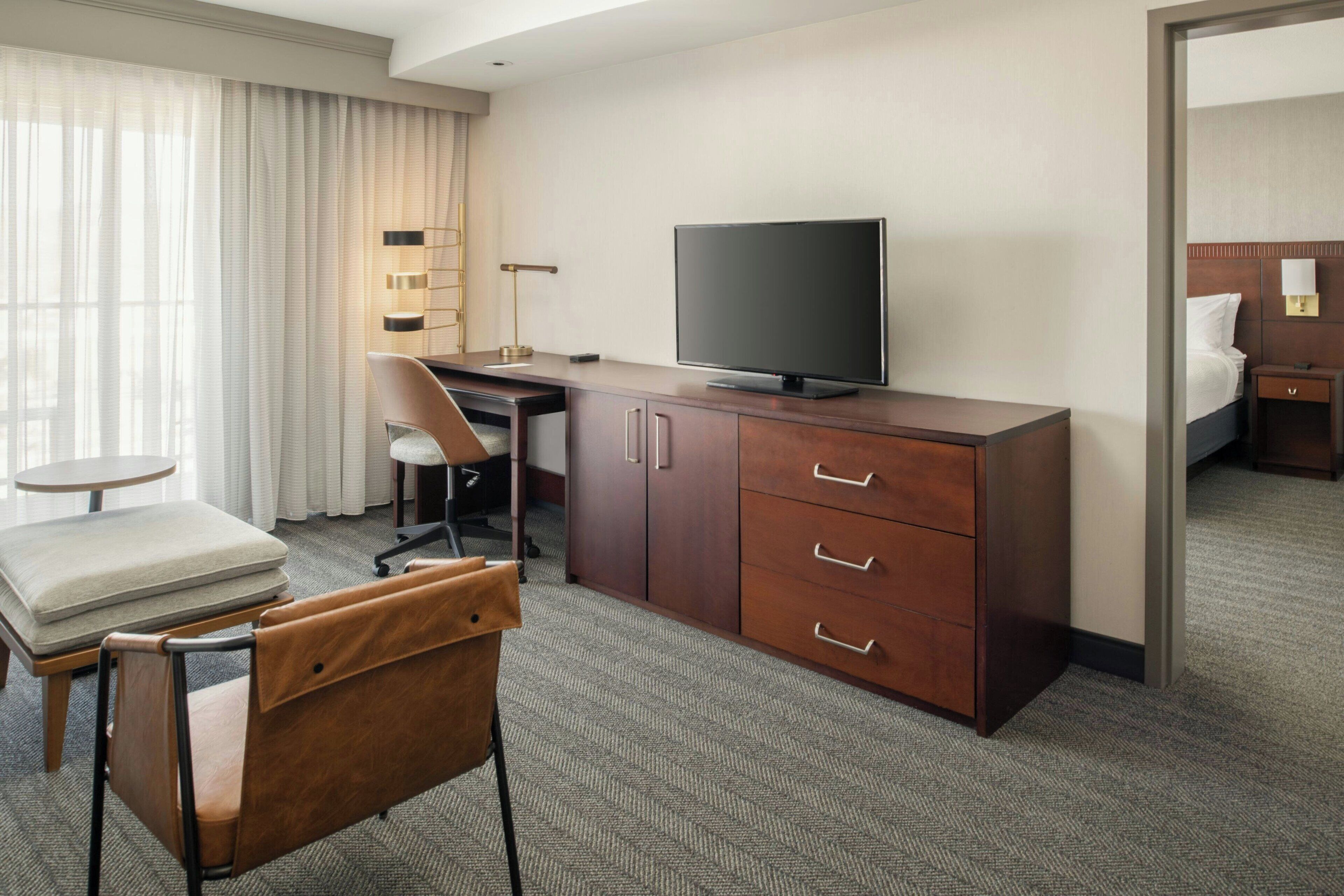 A hotel room with a desk, chair, television, and a bed.