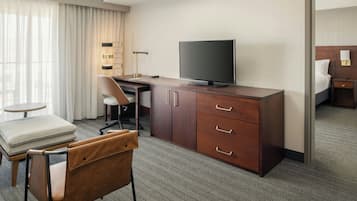 A hotel room with a desk, chair, television, and a bed.