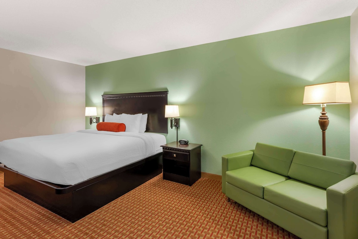 A hotel room with a bed, nightstand, lamp, and green sofa.