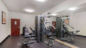 A gym with various exercise machines, a large mirror, and a door in the background.