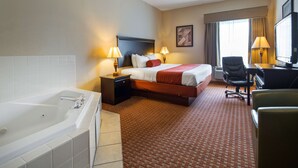 A hotel room with a large bed, a desk, a chair, a desk lamp, a TV, and a bathroom with a bathtub. - Best Western Plus Hopewell Fort Lee (Hopewell)
