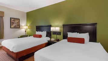 A hotel room with two beds, a desk, a chair, and a lamp.