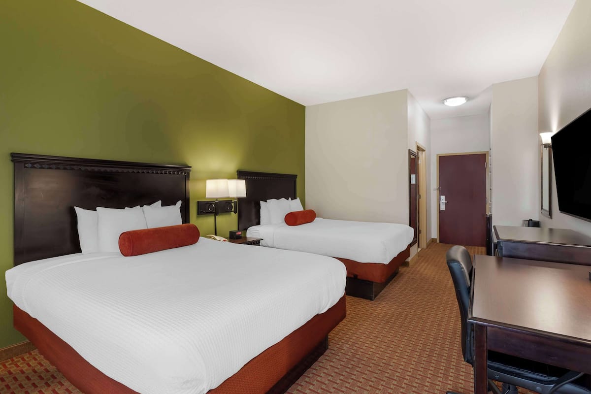 A hotel room with two beds, a desk, and a television.