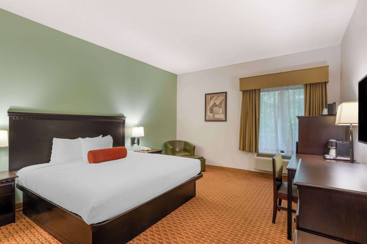 A hotel room with a large bed, a desk, a chair, a lamp, a telephone, and a window with curtains.