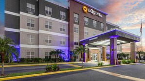 Un hôtel dont l’entrée est bien visible, avec une enseigne indiquant « LA QUIANTA », et une zone couverte soutenue par des piliers.