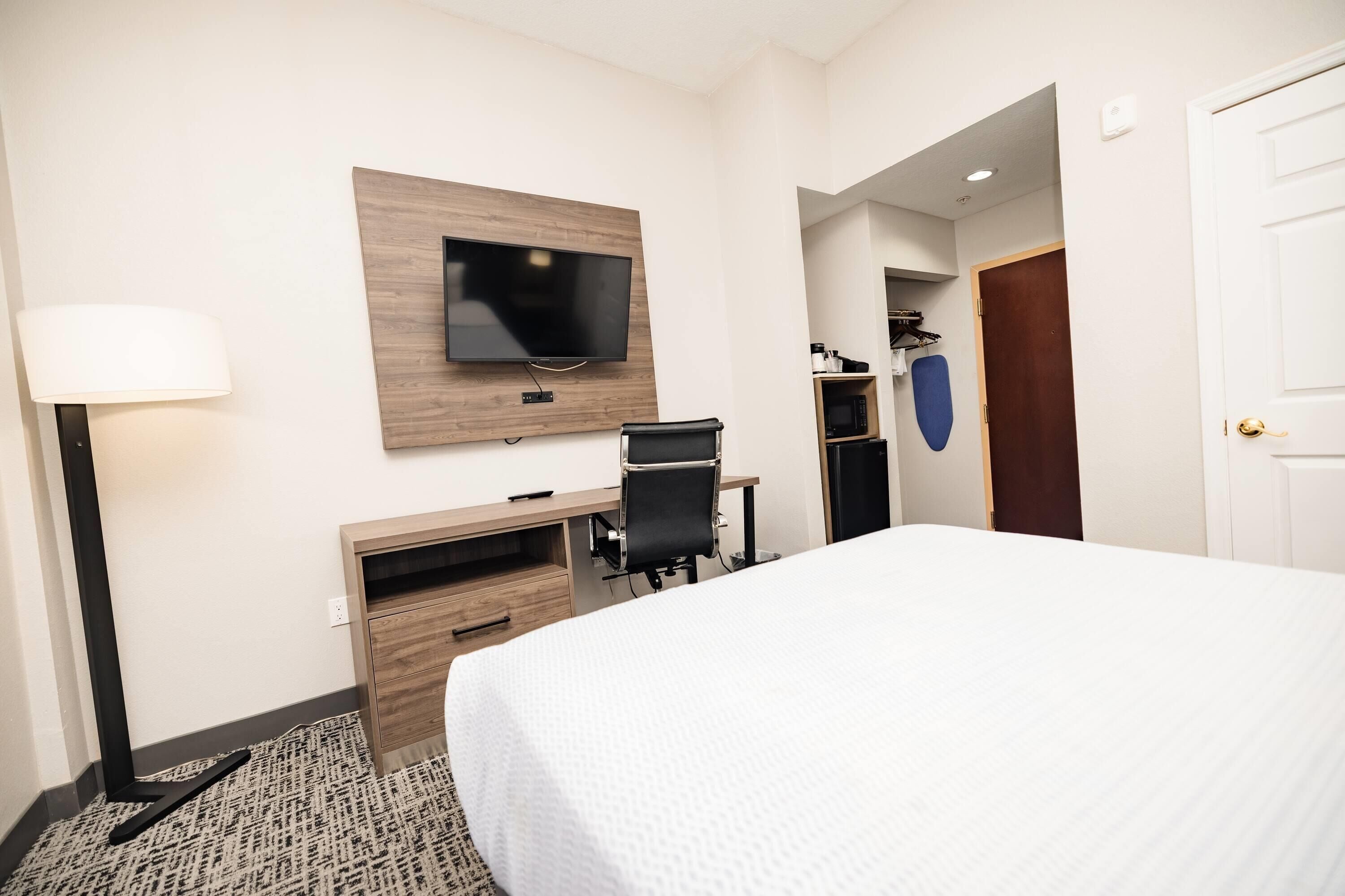 A hotel room with a bed, desk, chair, TV, lamp, and a door.
