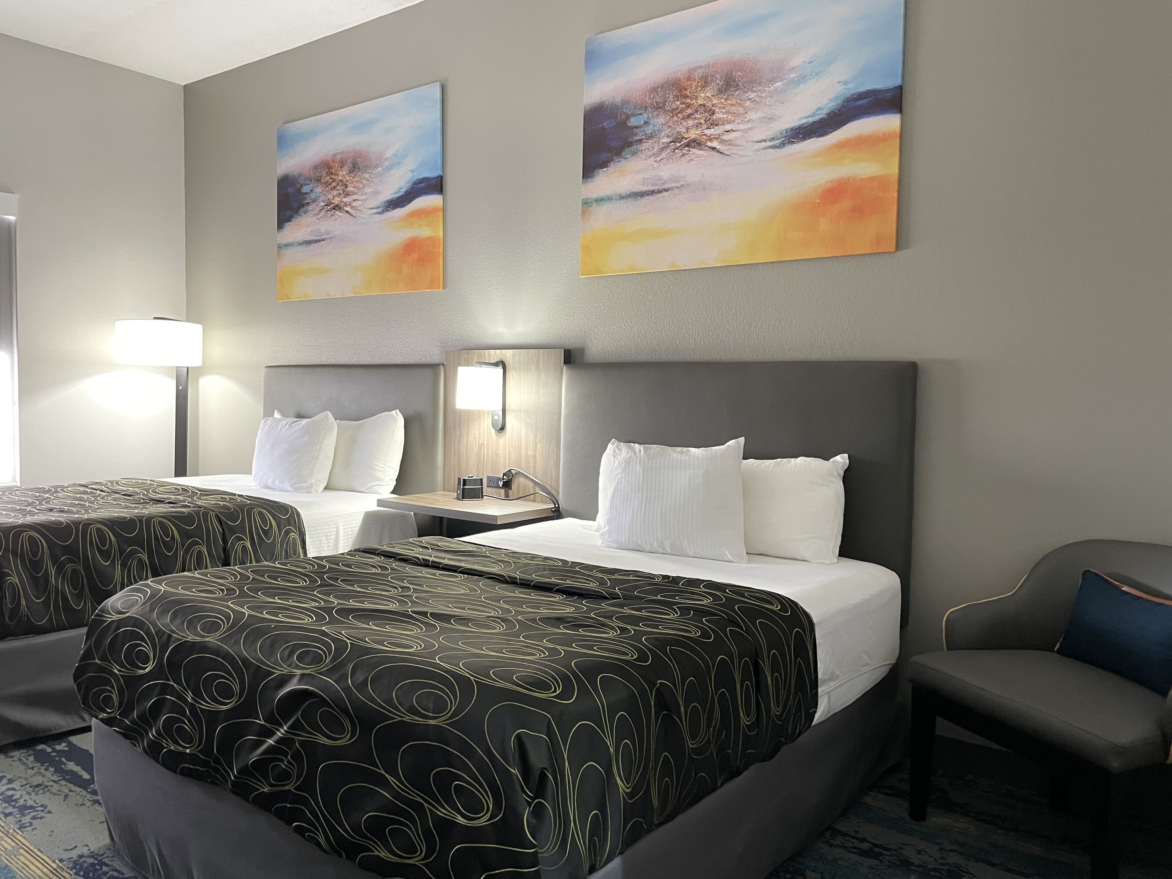 Une chambre d’hôtel avec deux lits, un bureau, une chaise et deux tableaux au mur.