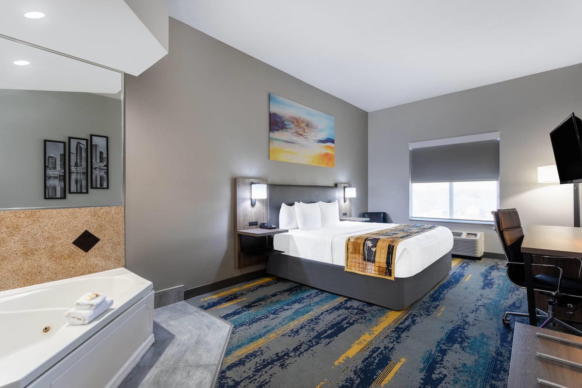 Ein Hotelzimmer mit einem großen Bett, einem Schreibtisch, einem Stuhl, einer Badewanne und einem Fenster.