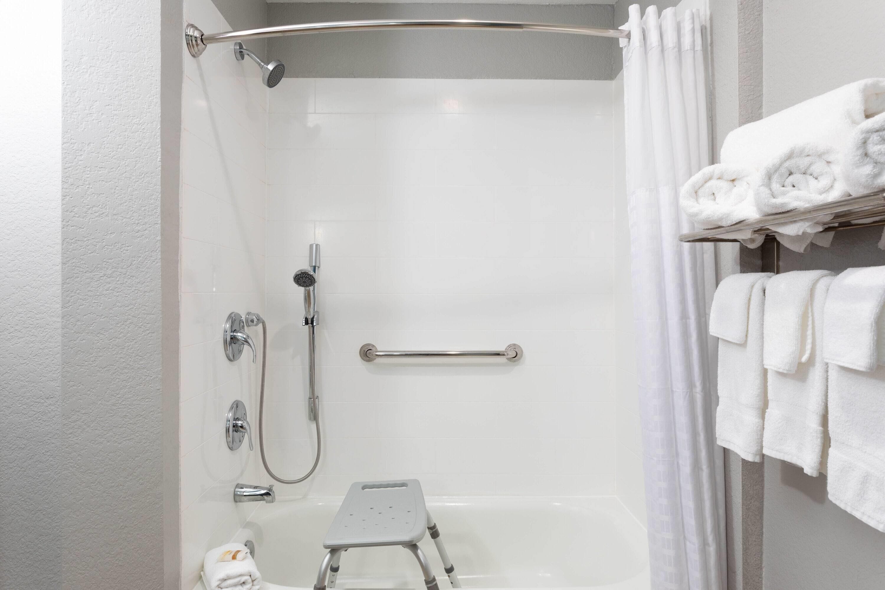 A shower area with a grab bar, a step stool, and a towel rack with folded towels.