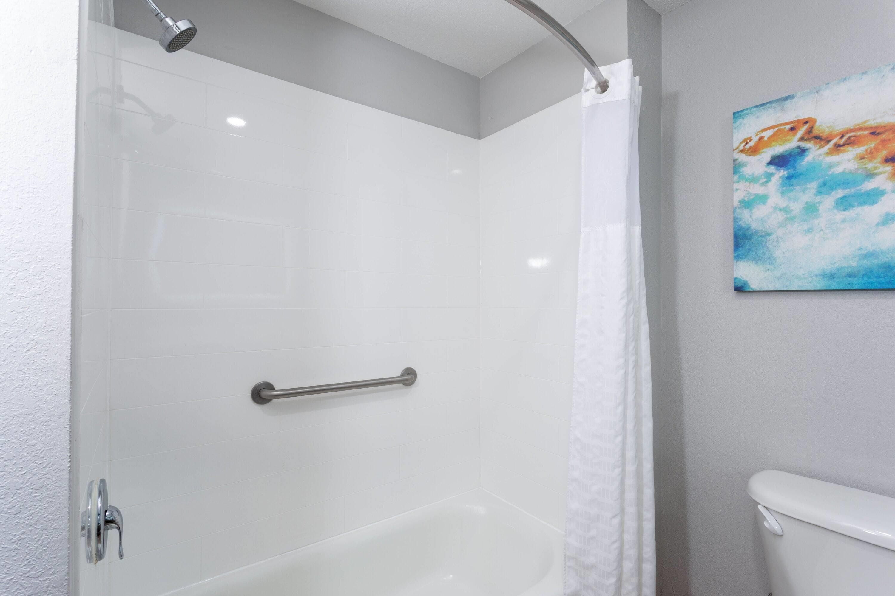 A shower with a glass door, a handrail, and a white curtain.