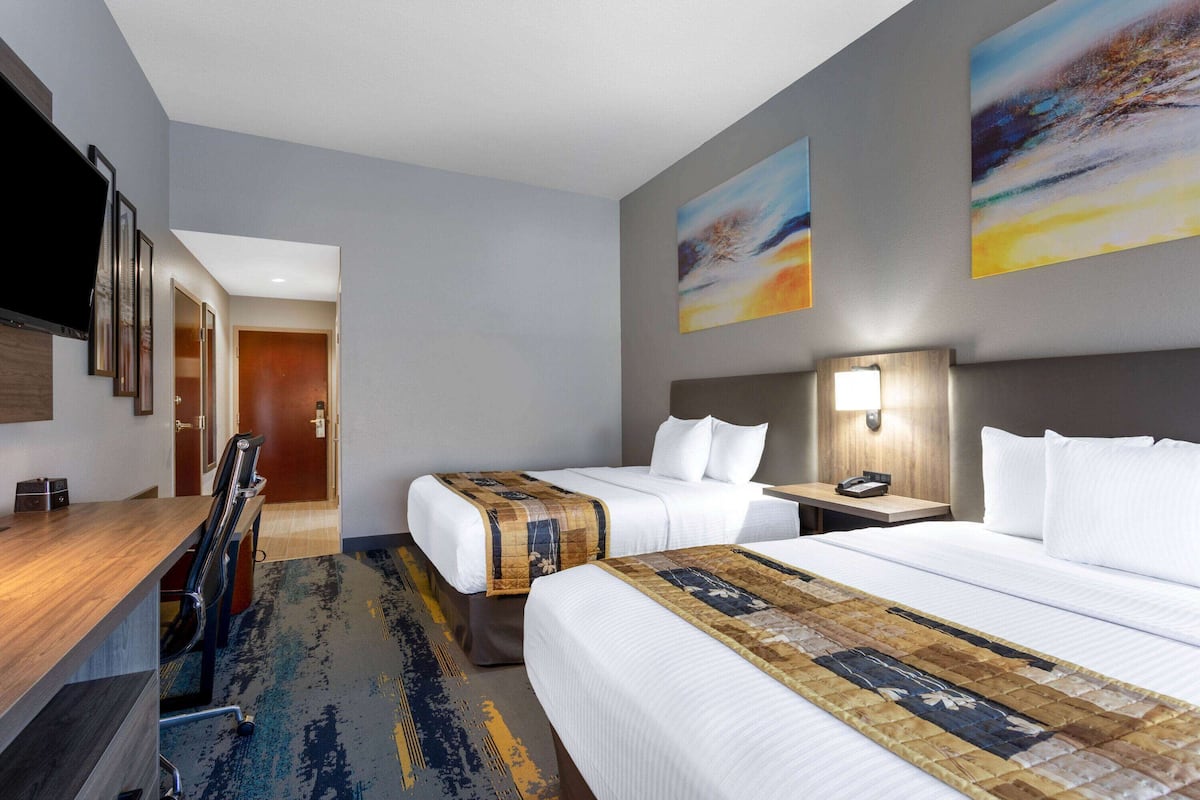 Ein Hotelzimmer mit zwei Betten, einem Schreibtisch, einem Stuhl, einem Fernseher und Bildern an den Wänden.