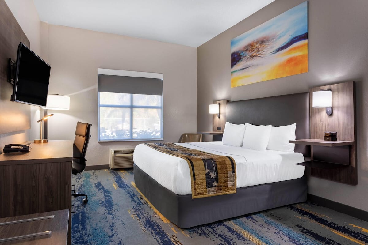 Ein Hotelzimmer mit Bett, Schreibtisch, Fernseher und einem Kunstwerk an der Wand.