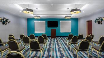 A conference room with a blue accent wall, a flat-screen TV, and a podium. Rows of chairs are arranged facing the TV.