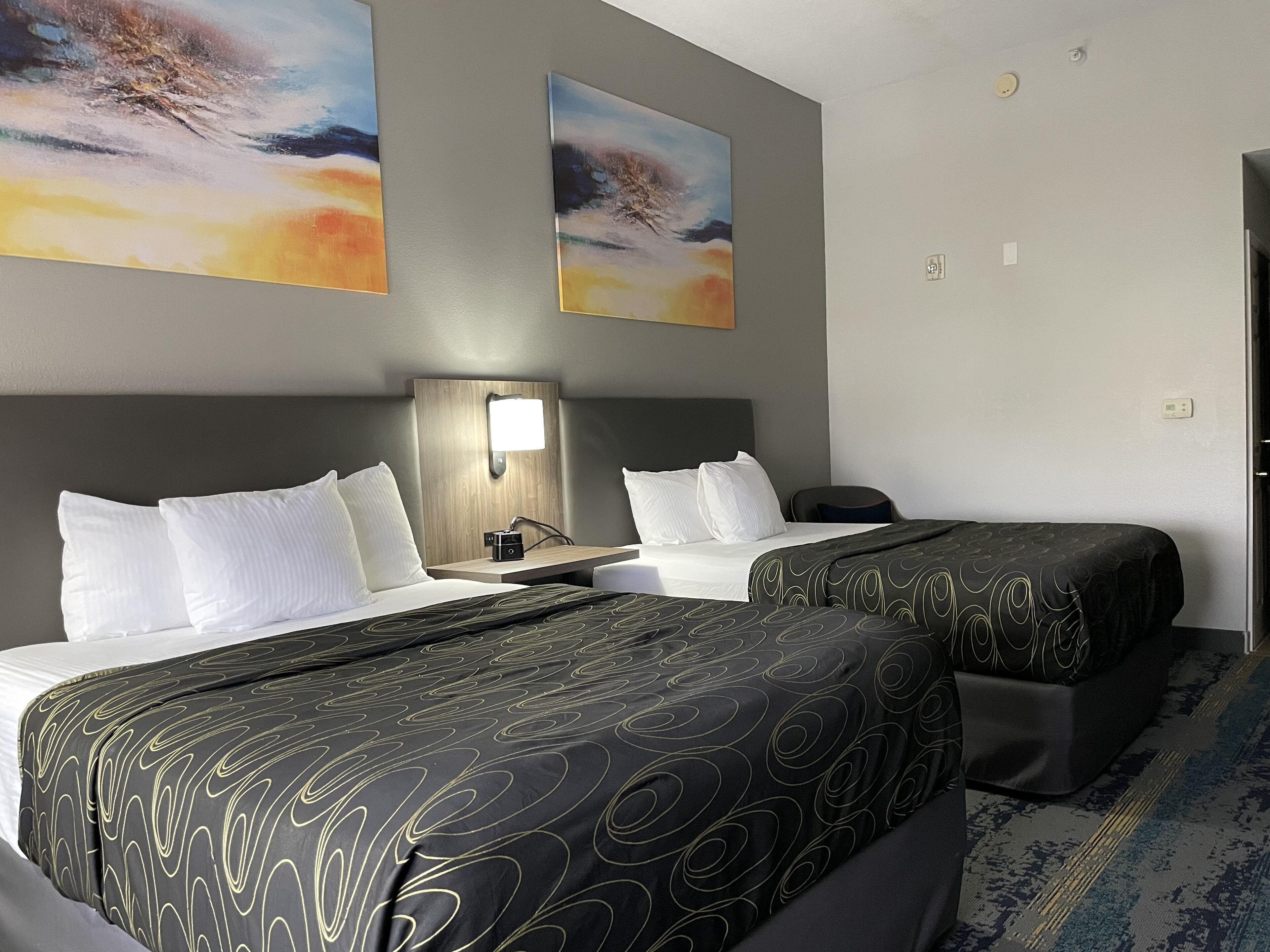 Habitació d'hotel amb dos llits, una tauleta de nit, una làmpada i dos quadres a la paret.