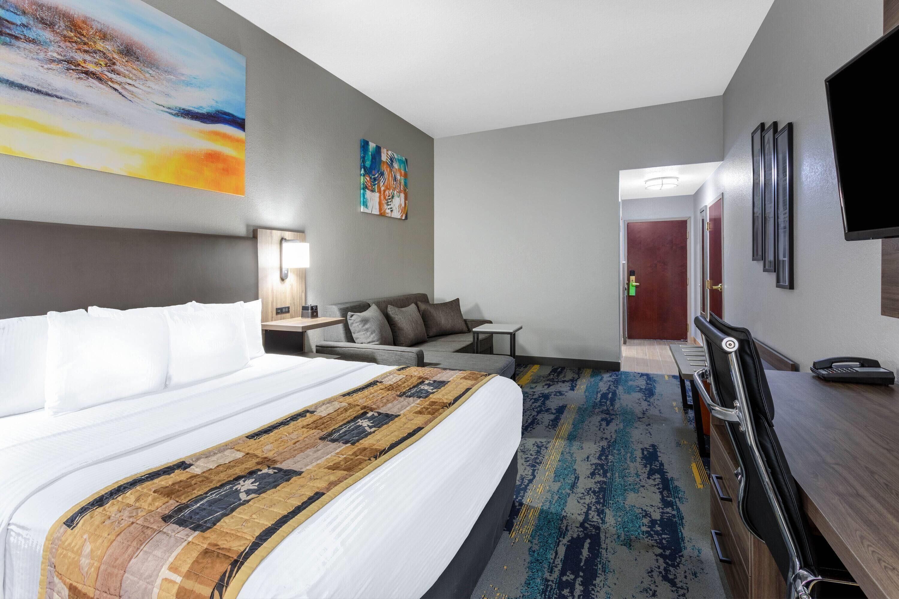 Habitación de hotel con una cama grande, un escritorio, un sofá, un televisor y obras de arte en las paredes.