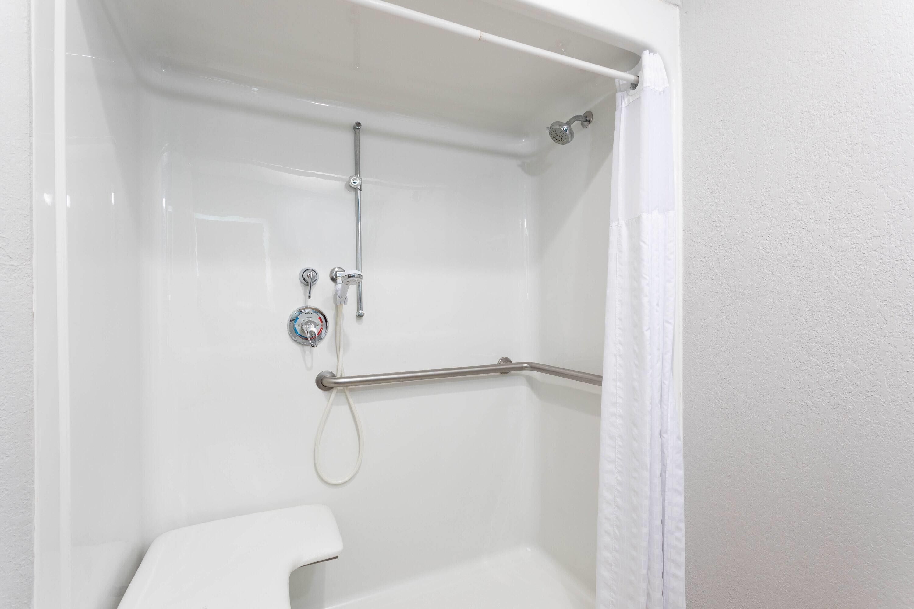 A white shower stall with a grab bar, a handheld showerhead, and a wall-mounted faucet.