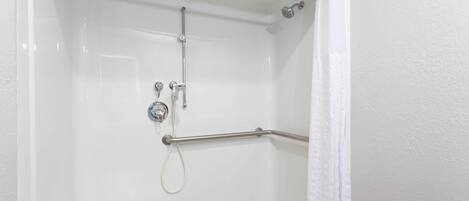 A white shower stall with a grab bar, a handheld showerhead, and a wall-mounted faucet.