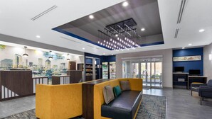 Un hall d’hôtel moderne avec un comptoir d’accueil, un canapé jaune et noir, un téléviseur et une grande fenêtre.