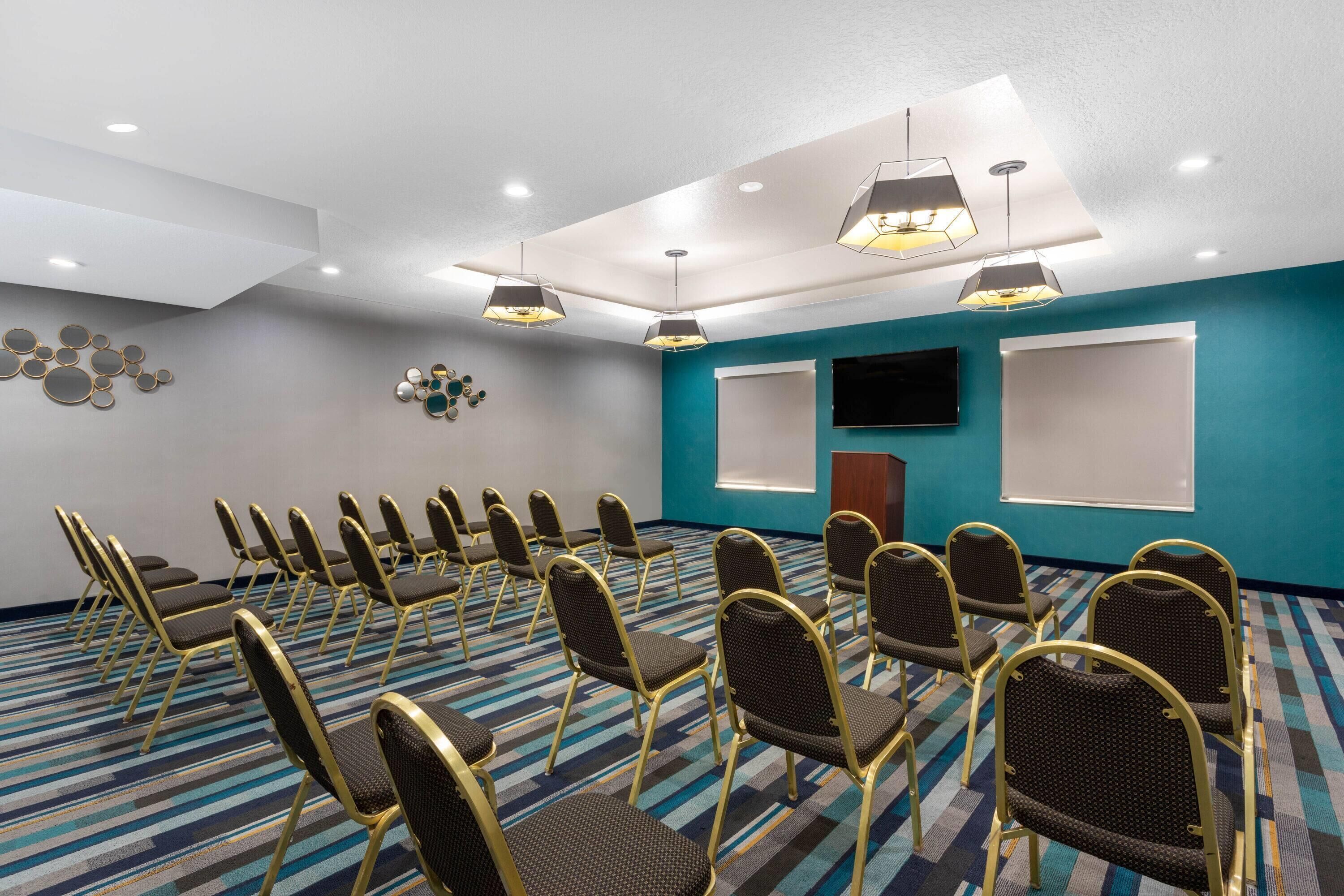 Une salle de conférence avec des rangées de chaises, un téléviseur à écran plat et un écran de projection.