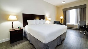 A hotel room with a large bed, two bedside tables with lamps, a chair, and a window with curtains.