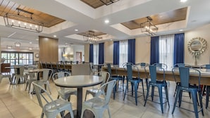 A spacious dining area with multiple tables and chairs, wooden ceiling beams, and modern lighting fixtures.
