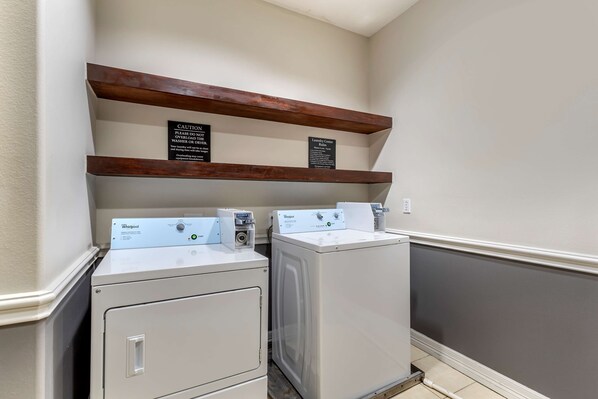 A laundry area with two Whirlpool washers and a caution sign.