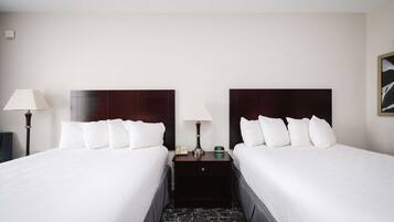 Habitación de hotel con dos camas, cada una con ropa de cama blanca y cabeceros oscuros. Hay mesitas de noche con lámparas y un reloj sobre una de ellas.