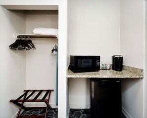 A compact kitchenette with a microwave, coffee maker, and a small refrigerator. There is a drying rack with clothes and a metal rack with shoes.
