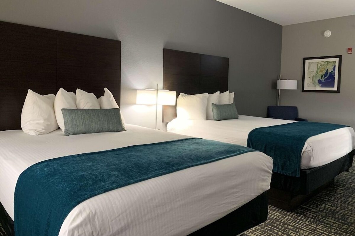 Hotelkamer met twee bedden, elk voorzien van witte lakens en kussens in teal. Er staan nachtlampjes en er hangt een lijstje aan de muur.