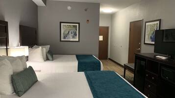 A hotel room with two beds, a desk, a TV, and artwork on the walls.