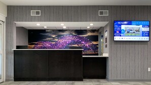 Uma área de recepção com design moderno, apresentando uma grande tela digital exibindo informações do hotel, um balcão de recepção e um mural de uma ponte à noite.