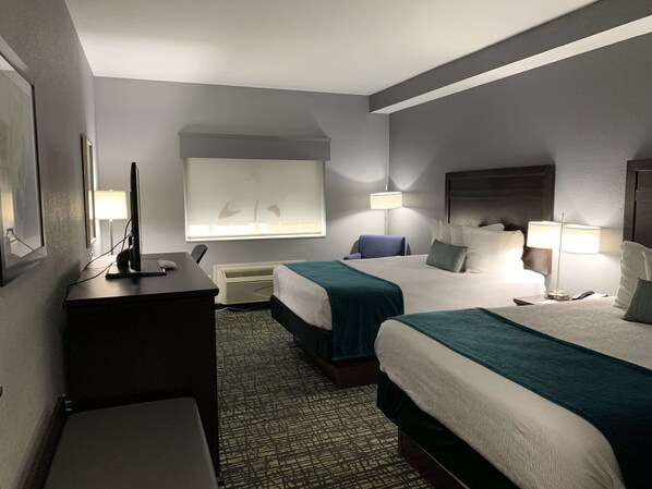 Habitación de hotel con dos camas, un escritorio, una silla, un televisor y una ventana con persianas.