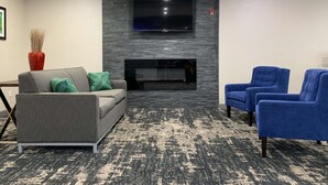Uma sala de estar moderna com um sofá cinzento, duas poltronas azuis, uma TV de tela plana fixada numa parede de pedra e uma lareira.