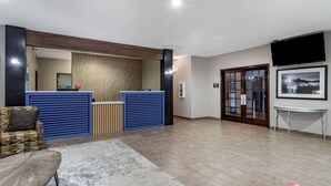 A reception area with a blue counter, a wooden reception desk, a framed picture on the wall, and a tiled floor.