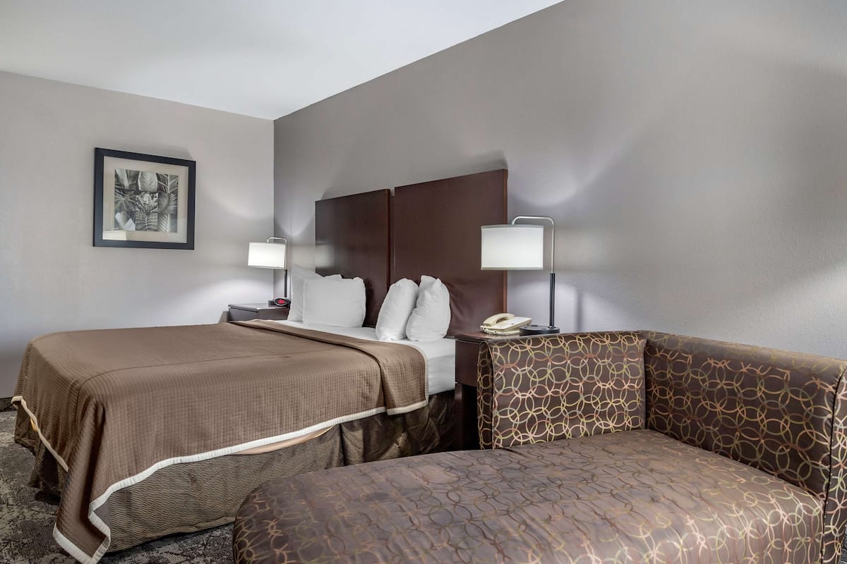 A hotel room with two beds, a sofa, a nightstand with a lamp, and a framed picture on the wall.