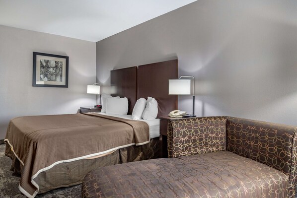 A hotel room with two beds, a sofa, a nightstand with a lamp, and a framed picture on the wall. - Best Western Oakdale Inn (Oakdale)