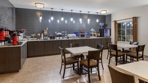 A modern kitchen with a central island, overhead lighting, and a dining area with chairs and a table.