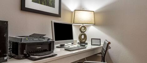 A hotel workspace with a desktop computer, printer, and lamp.
