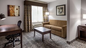 A hotel room with a wooden desk, a sofa, a coffee table, and a large window with curtains.