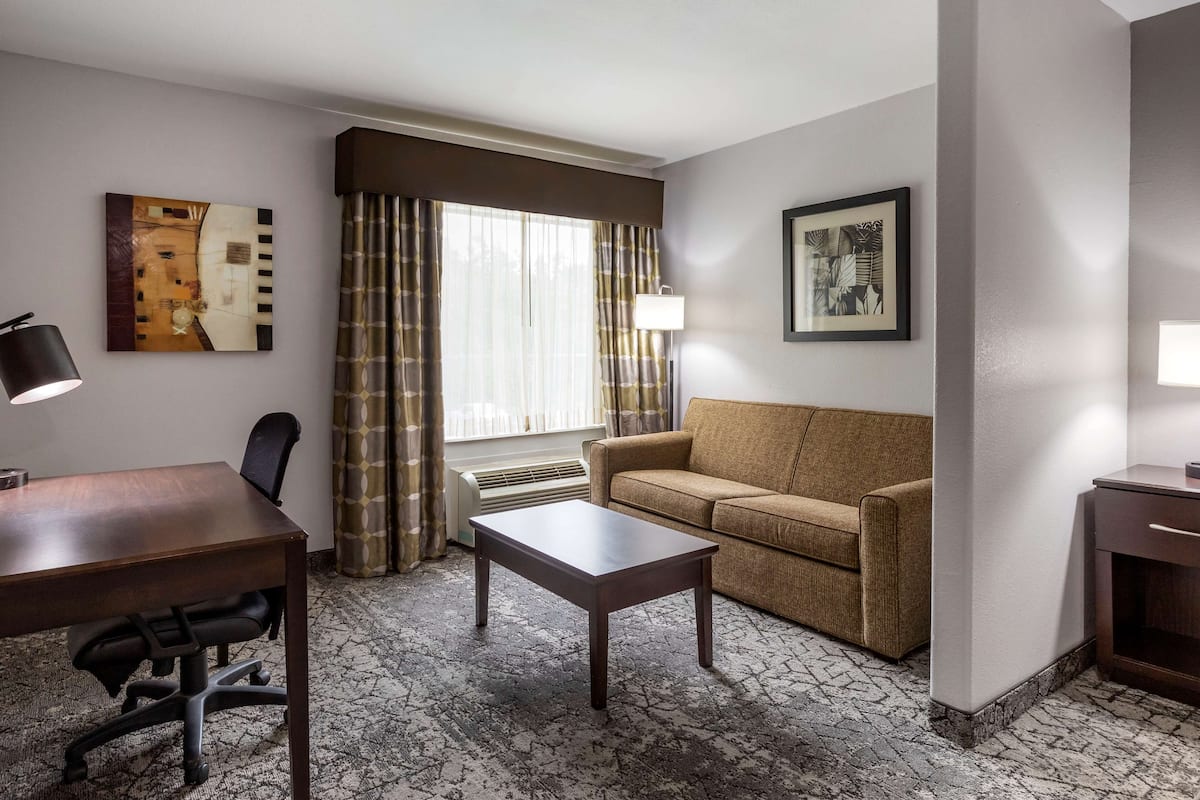A hotel room with a wooden desk, a sofa, a coffee table, and a large window with curtains.